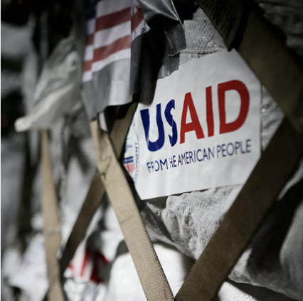 USAID logo with community gathering in the background