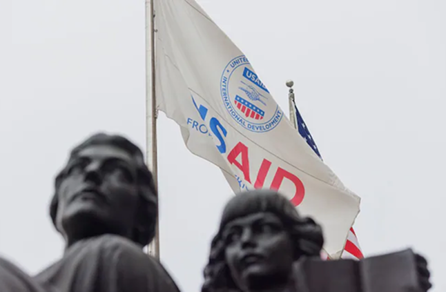 USAID flag waving prominently against bright blue sky